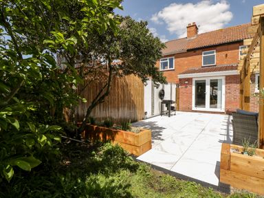 A backyard with tiled patio wooden planters trees and a barbecue at Seacider in Burnham-On-Sea