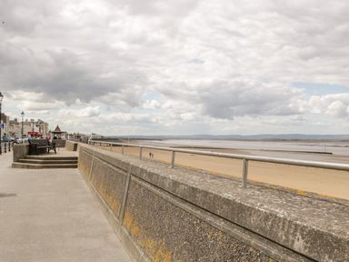 A concrete promenade with benches and railings next to a sandy beach and cloudy sky at Seacider in Burnham-On-Sea