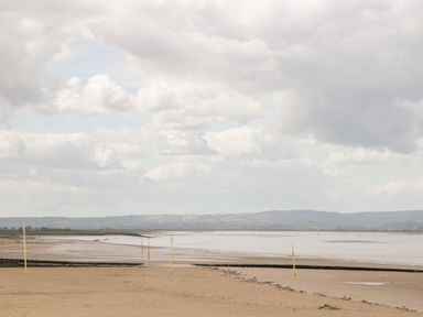 A beach with sand, water, and yellow poles with hills and clouds in the background at Seacider in Burnham-On-Sea