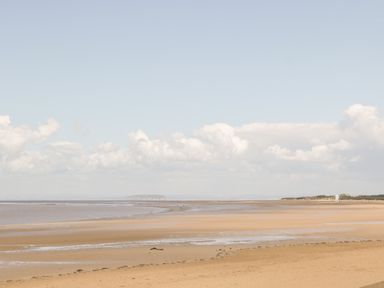 A sandy beach with shallow water and a small white building in the distance at Seacider in Burnham-On-Sea