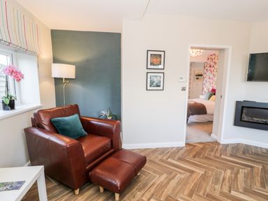 A living room with a brown leather armchair and ottoman a floor lamp and a window with striped blinds at The Chalet in Benllech