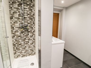 A bathroom with a shower area with patterned tiles and a sink next to a wooden door at The Chalet in Benllech