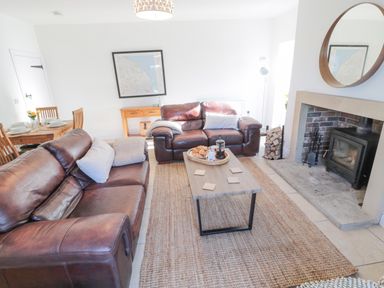 A living room with two brown leather sofas a wooden coffee table a fireplace with firewood and a round mirror on the wall at Little Haven in Bamburgh