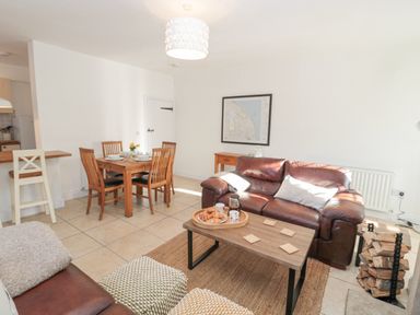 A living room with a brown leather sofa a wooden coffee table with croissants and mugs a dining table with chairs and place settings at Little Haven in Bamburgh