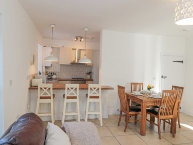 An open kitchen and dining area with wooden chairs and a dining table and three stools at a kitchen counter at Little Haven in Bamburgh