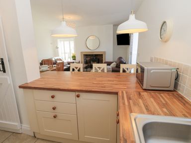 A kitchen countertop with a microwave and sink overlooking a dining area with chairs and a living room with sofas and a fireplace at Little Haven in Bamburgh