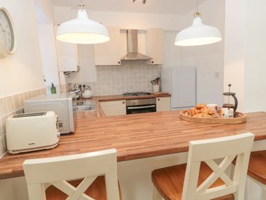 A kitchen with wooden countertops white cabinets and two chairs at Little Haven in Bamburgh