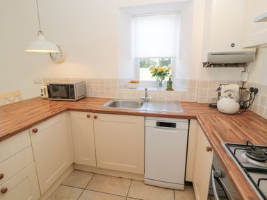 A kitchen with wooden countertops a sink a dishwasher a microwave and a window with flowers on the sill at Little Haven in Bamburgh