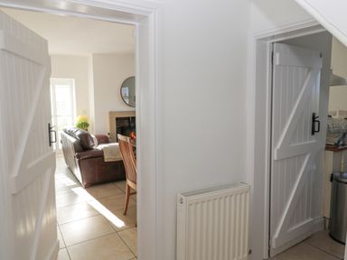 A view through white doors into a living room with a brown leather sofa a wooden chair a fireplace with a fire and a window with flowers at Little Haven Bamburgh