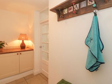 Hallway with a cabinet and lamp next to a door and a wall-mounted wooden coat rack with a blue towel at Little Haven in Bamburgh
