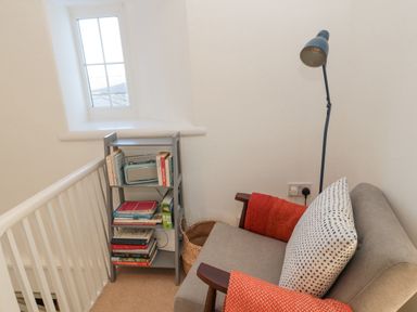 A small reading nook with a grey armchair a polka dot cushion an orange throw a floor lamp and a bookshelf with books at Little Haven in Bamburgh