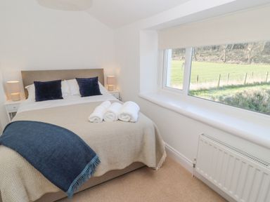 A bedroom with a bed with beige and blue bedding and two bedside tables with lamps at Little Haven Bamburgh