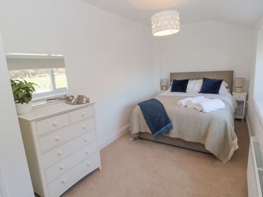 A bedroom with a bed featuring pillows and towels bedside tables with lamps a dresser with a plant and a window at Little Haven in Bamburgh