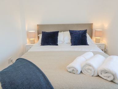 A bedroom with a bed with beige cover two blue pillows and three rolled white towels at Little Haven in Bamburgh