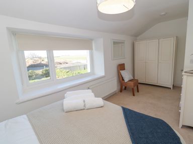 A bedroom with a bed, towels on the bed, a window with a blind, a wicker chair with a cushion, a mirror on the wall, and a wardrobe at Little Haven in Bamburgh