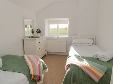 A bedroom with two single beds a dresser with a mirror and a window at Little Haven in Bamburgh