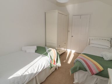 A bedroom with two single beds white bedding green throws and a white wardrobe at Little Haven Bamburgh