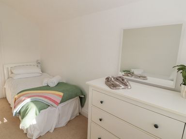 A bedroom with a single bed with white bedding and a green blanket and a dresser with a mirror at Little Haven in Bamburgh