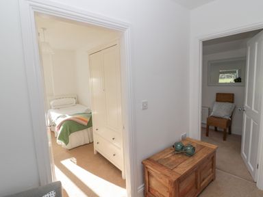 A hallway with wooden chest and two adjacent rooms one with a single bed and wardrobe and the other with a wicker chair at Little Haven in Bamburgh