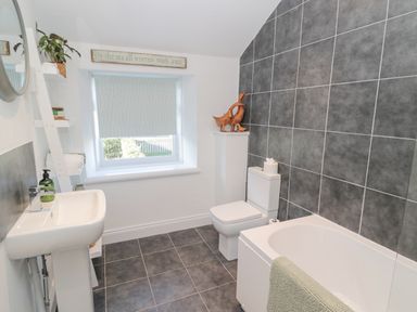 A bathroom with a bathtub a toilet a sink shelves and a window with a blind at Little Haven in Bamburgh