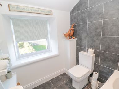 A bathroom with a white toilet gray tiled walls and decorative wooden ducks on a white pillar at Little Haven in Bamburgh