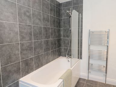 A bathroom with a bathtub shower combination and a towel rail at Little Haven in Bamburgh