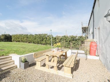 An outdoor seating area with wooden picnic table and benches on gravel near a lawn and shrubs at Little Haven Bamburgh