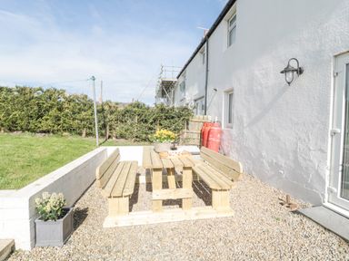 An outdoor area with a wooden picnic table and benches on gravel beside a white building with a light fixture at Little Haven in Bamburgh