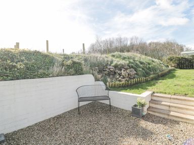 An outdoor seating area with a metal bench gravel ground a small planter and steps leading to a grassy area at Little Haven in Bamburgh