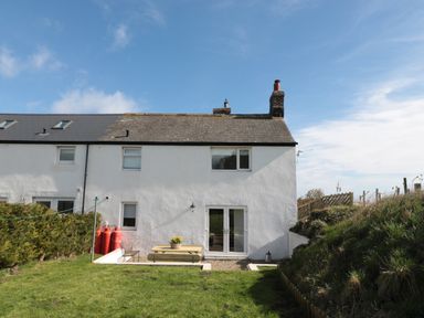A white two-story house with a sloped roof a small patio area with a picnic table and flower pot and a grass lawn at Little Haven in Bamburgh