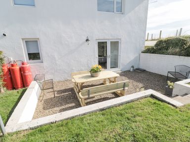 An outdoor patio area with a wooden picnic table and benches two metal chairs red gas cylinders and a white building at Little Haven in Bamburgh