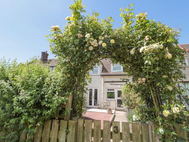 A garden arch with climbing roses over a wooden gate and patio furniture at 3 St Cuthberts Garth in Bamburgh