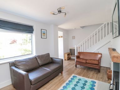 A living room with two leather sofas a staircase and a window at 3 St Cuthberts Garth in Bamburgh