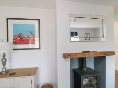 A framed painting of a person in a red car above a lamp and cabinet next to a fireplace with a mirror above it at 3 St Cuthberts Garth in Bamburgh