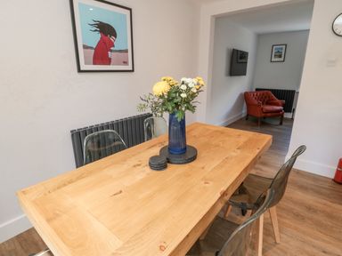 A dining room with a wooden table and flowers in a vase at 3 St Cuthberts Garth in Bamburgh