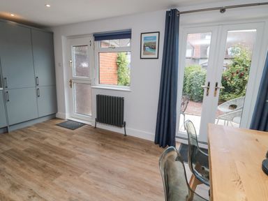 A kitchen area with blue cabinets a wooden floor a glass door with blue curtains and a wooden table with chairs at 3 St Cuthberts Garth Bamburgh