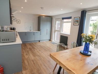 A kitchen with grey cabinets a wooden dining table with flowers in a blue vase and wooden floor at 3 St Cuthberts Garth Bamburgh