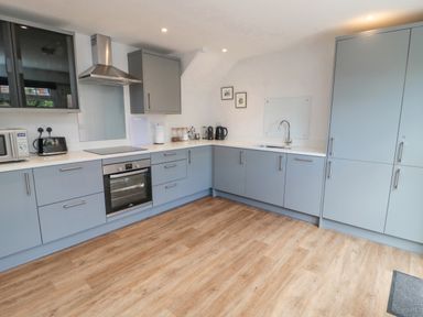 A kitchen with grey cabinets an oven a sink and wooden flooring at 3 St Cuthberts Garth Bamburgh