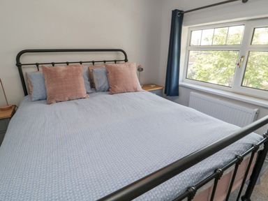 A bedroom with a double bed with blue bedding and pink pillows beside a window with blue curtains at 3 St Cuthberts Garth in Bamburgh