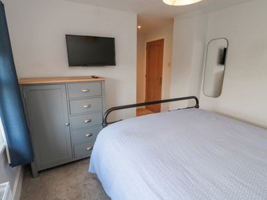 A bedroom with a bed a grey chest of drawers a wall mounted TV and a mirror at 3 St Cuthberts Garth in Bamburgh