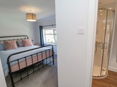 A bedroom with a black metal bed frame and window next to a bathroom with a glass shower at 3 St Cuthberts Garth Bamburgh