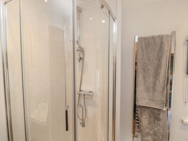 A shower cabin with glass doors and a towel rack with gray towels in a bathroom at 3 St Cuthberts Garth in Bamburgh