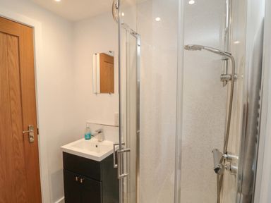 A bathroom with a wooden door a sink with a cabinet a mirror and a shower with a glass door at 3 St Cuthberts Garth in Bamburgh