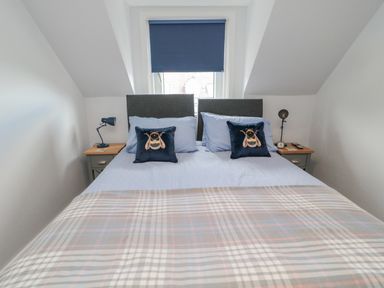 A bedroom with a double bed decorated with bee pillows and a window with a blue blind at 3 St Cuthberts Garth in Bamburgh