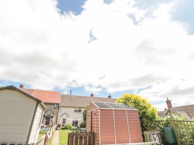 A backyard with storage sheds garden furniture and houses in the background at 3 St Cuthberts Garth Bamburgh