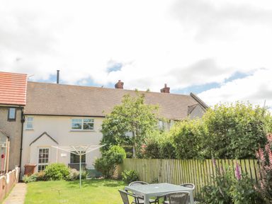 A backyard garden with a table and chairs a clothes drying rack bushes and trees at 3 St Cuthberts Garth in Bamburgh