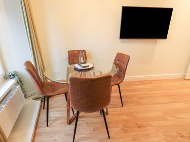 A dining area with a round glass table surrounded by four brown chairs and a wall-mounted TV at Windermere Crescent in Windermere