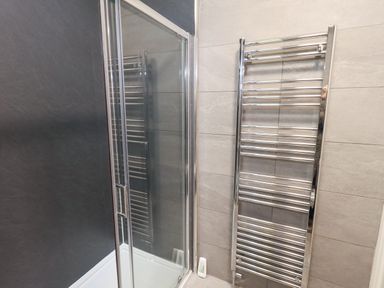 A bathroom with a glass shower enclosure and a chrome heated towel rail on a tiled wall at Windermere Crescent in Windermere