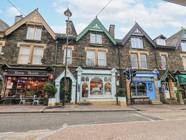 A row of stone buildings with shops and cafes on a street at Windermere Crescent in Windermere