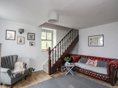 A living room with a red leather sofa, grey armchair, wooden staircase, and wall art at Bethania Llangoed near Beaumaris